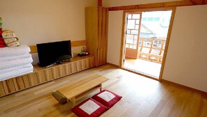 Una stanza con pavimento in legno, un televisore su una bassa mensola, un letto con biancheria da letto bianca e un cuscino rosso e bianco sul pavimento.
