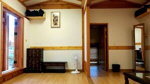 Una stanza con pavimento in legno, una ventola portatile, un'opera d'arte incorniciata al muro e una panca in legno.