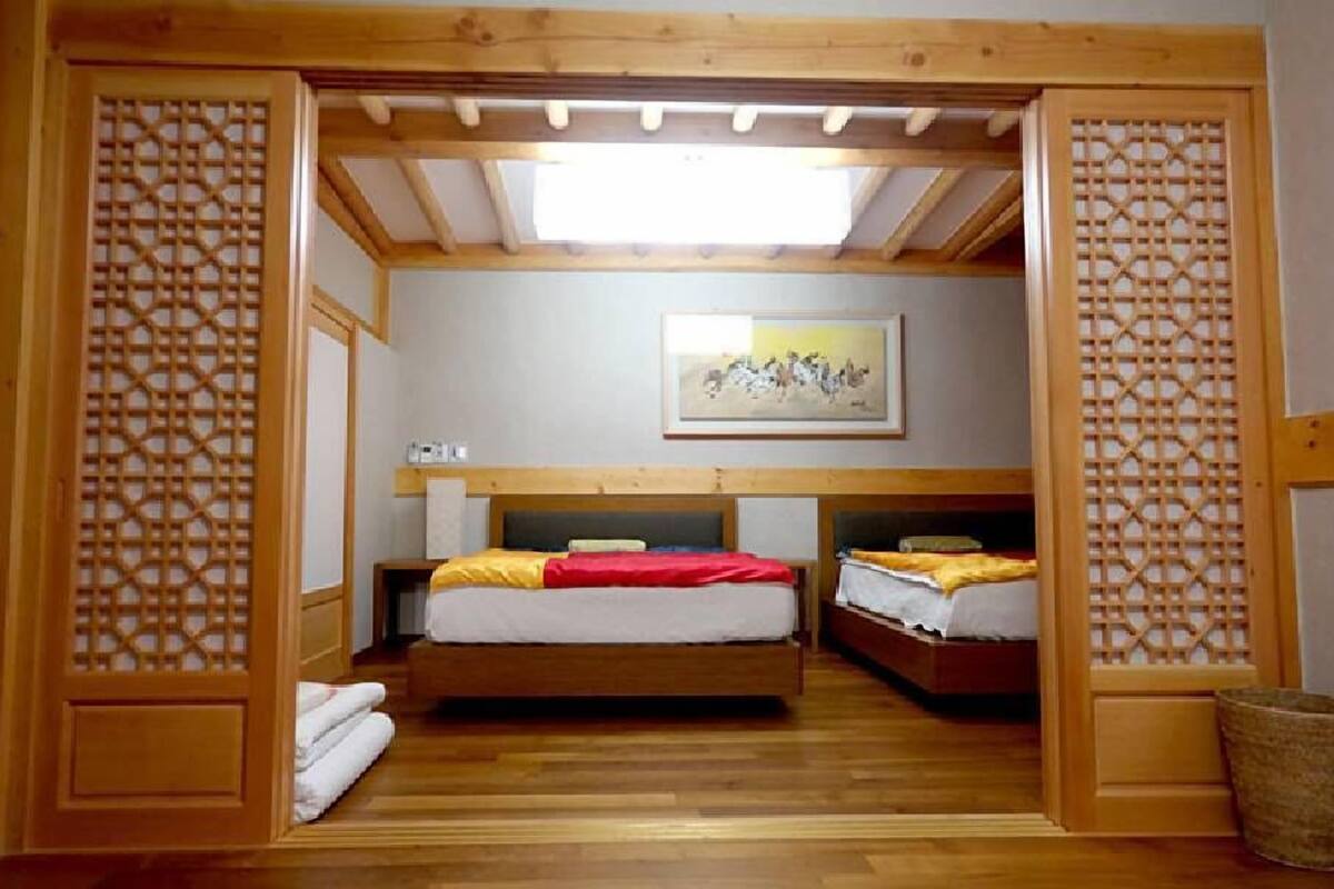 Quarto com duas camas, vigas de madeira, claraboia e um quadro na parede.