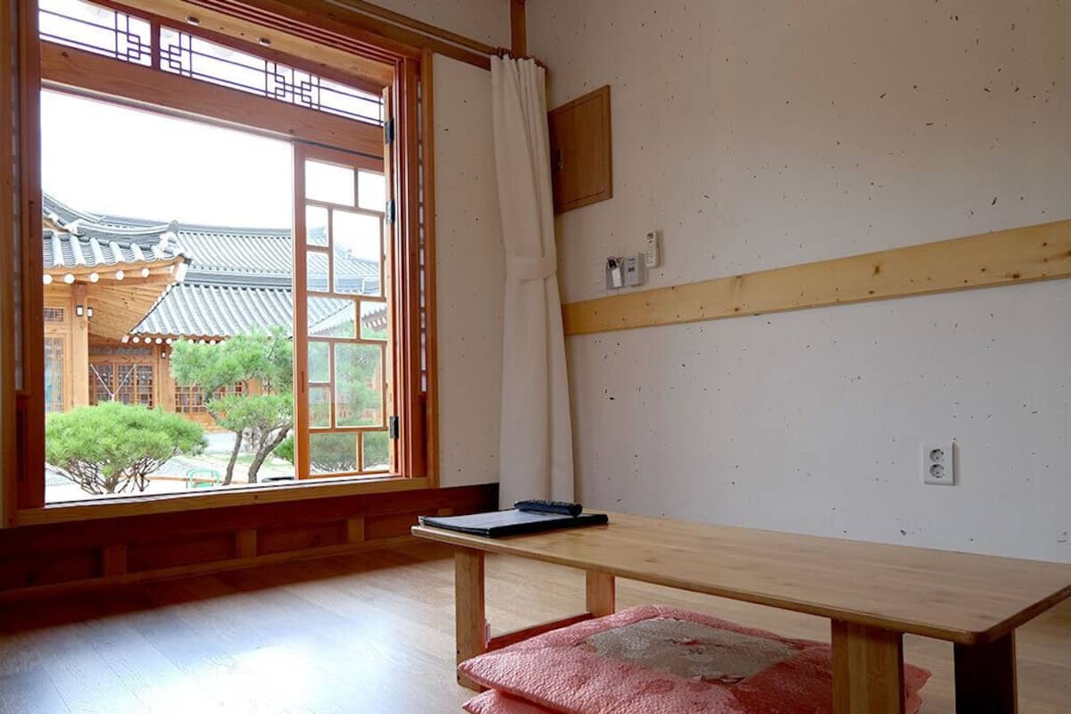 Quarto com um banco de madeira, janela com vista para arquitetura tradicional e uma pequena mesa com um caderno e caneta.