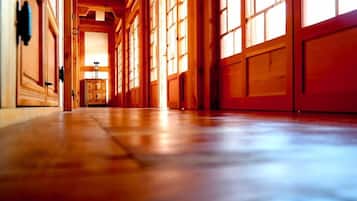 A hallway with wooden floors and large windows, leading to a room with a wooden cabinet.