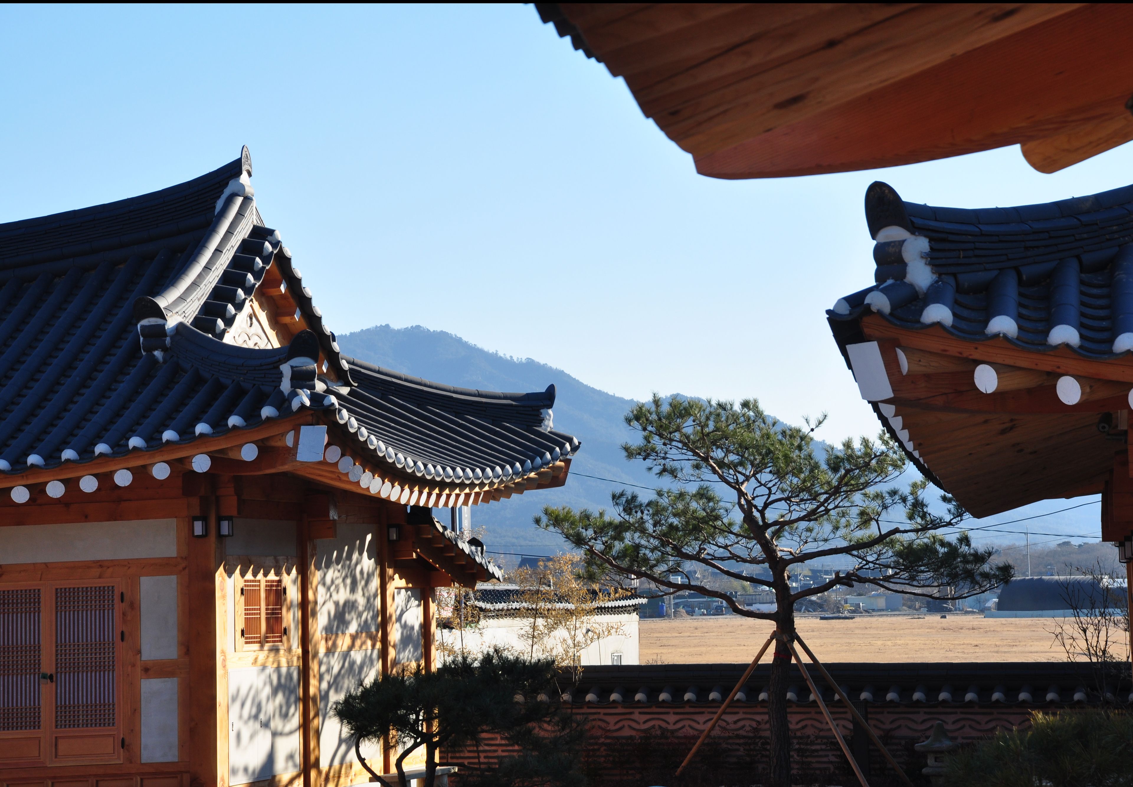 Traditional Korean architecture with wooden structures and tiled roofs, set against a mountainous backdrop.