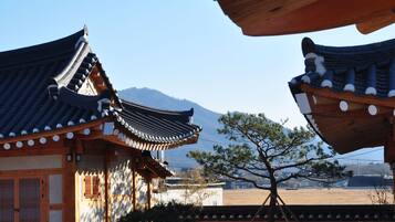 Traditional Korean architecture with wooden structures and tiled roofs, set against a mountainous backdrop.