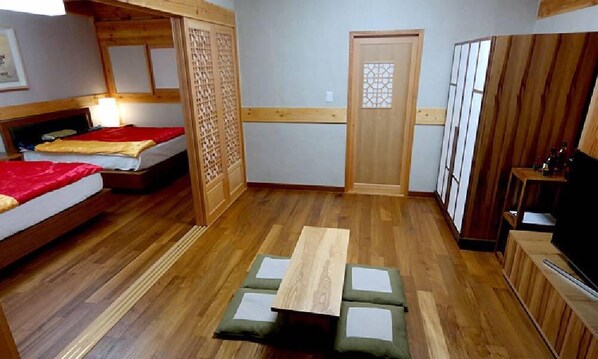 A room with two beds, a wooden floor, a small table with cushions, a TV, and a door with a lattice design. - Gyeongju Hwangnamkwan Hanok Hotel (Gyeongju)