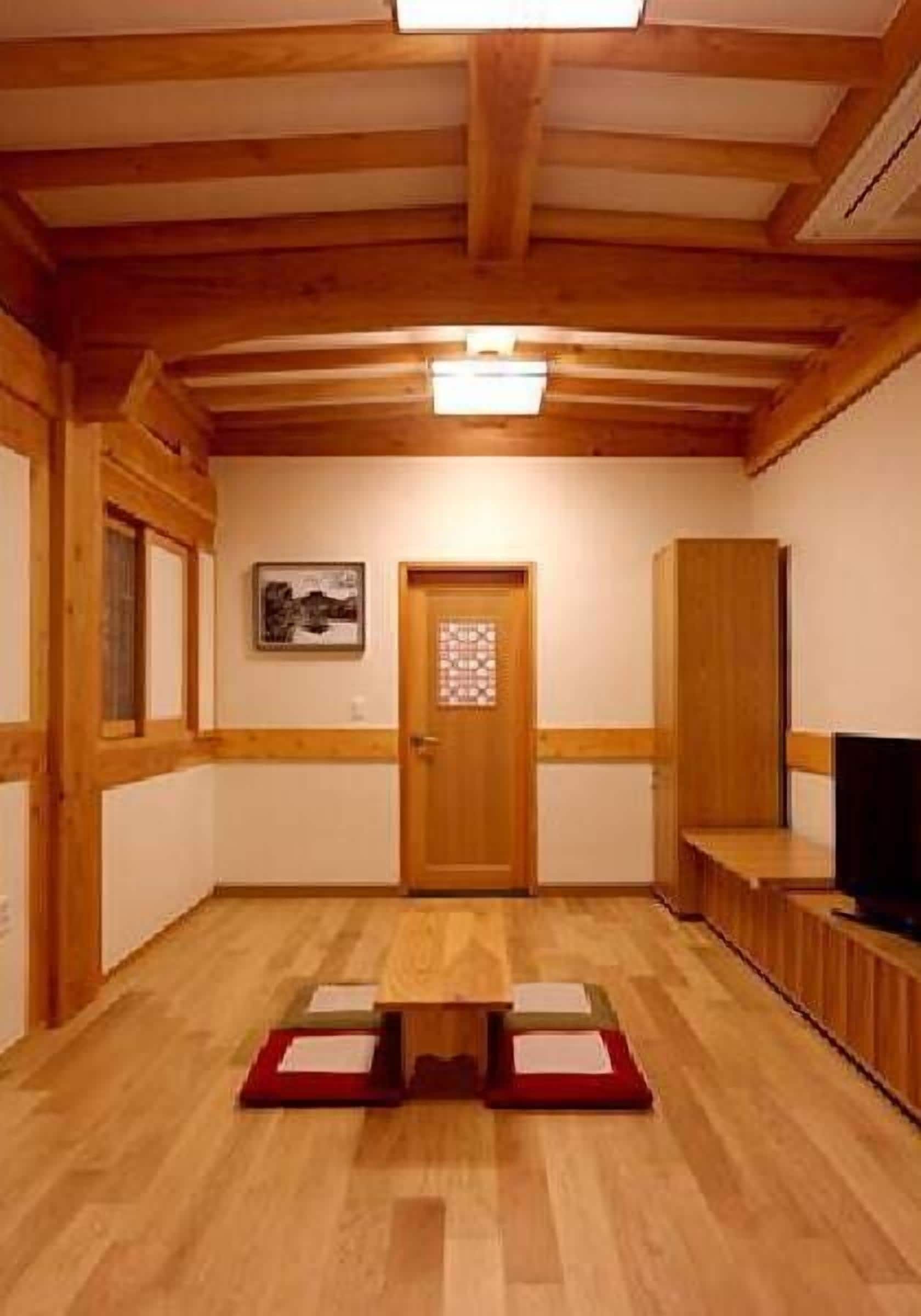 A room with a wooden ceiling, a door with a window, a framed picture on the wall, and a television on a stand.