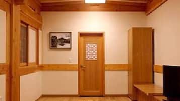 A room with a wooden ceiling, a door with a window, a framed picture on the wall, and a television on a stand.