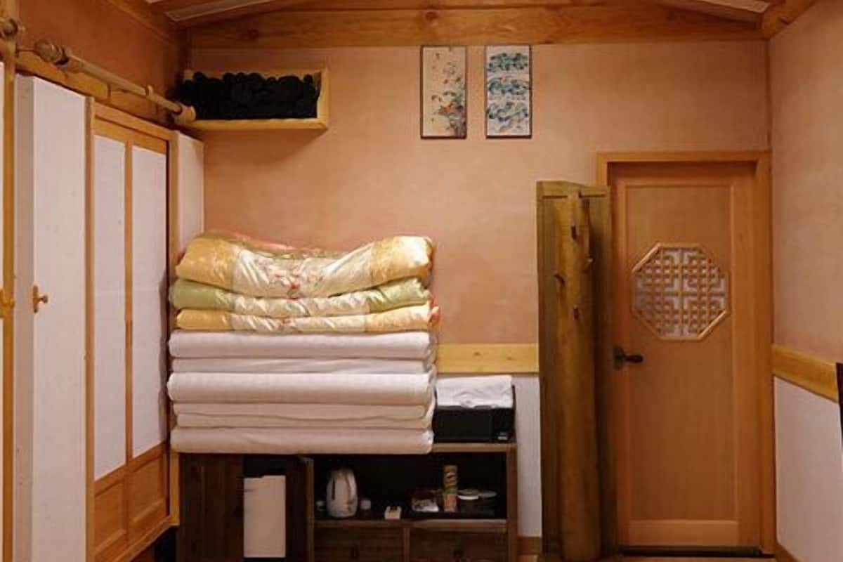 Quarto compacto com cama, porta de madeira e uma pequena prateleira com objetos.