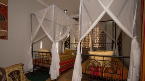 A room with two beds, each with a canopy. There is a patterned wall hanging on the left and a patterned curtain on the window. - Korona Villa Bed & Breakfast (Arusha)