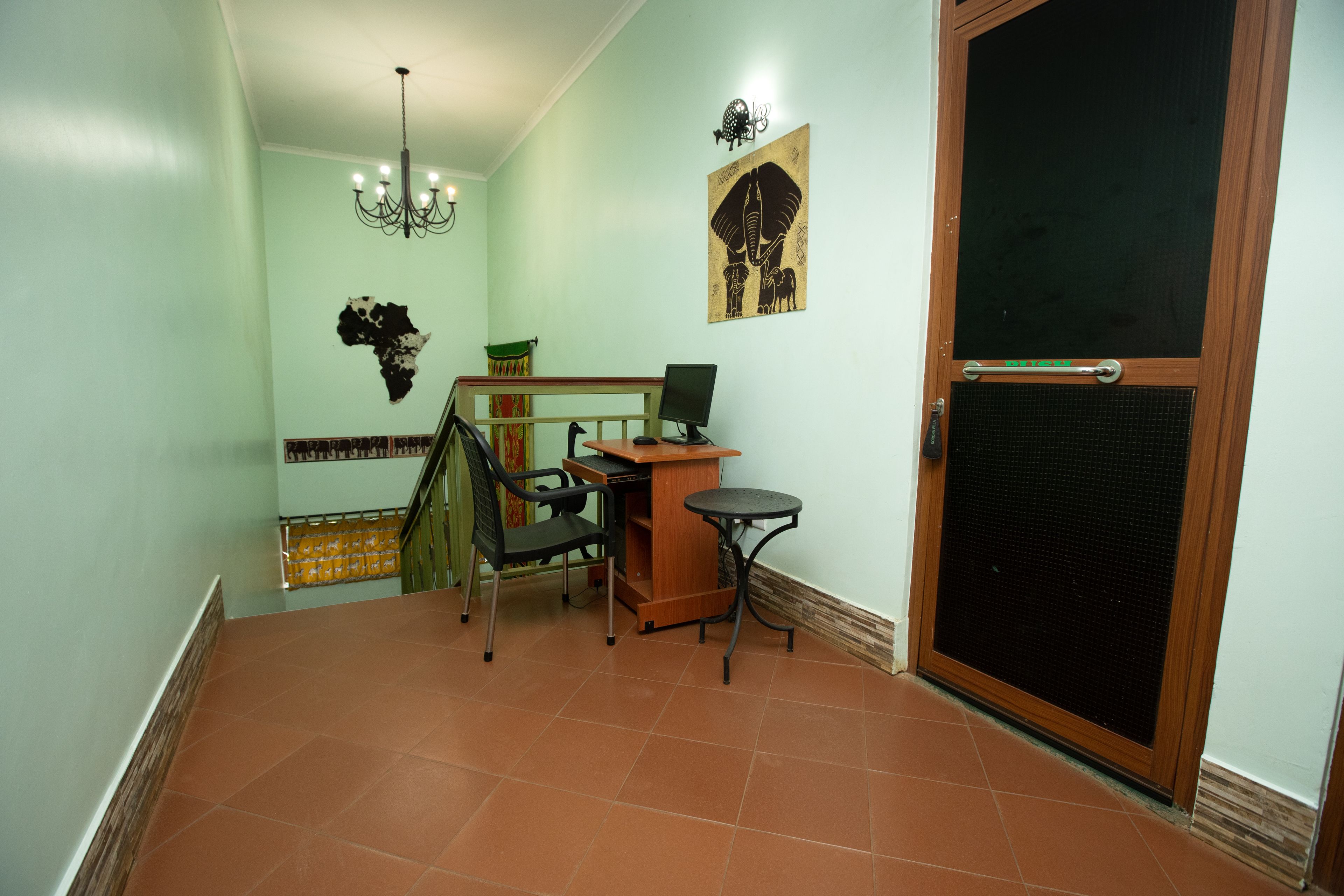 Une pièce comprenant un bureau, une chaise et un ordinateur, un escalier et une porte dotée d’une grille de sécurité.