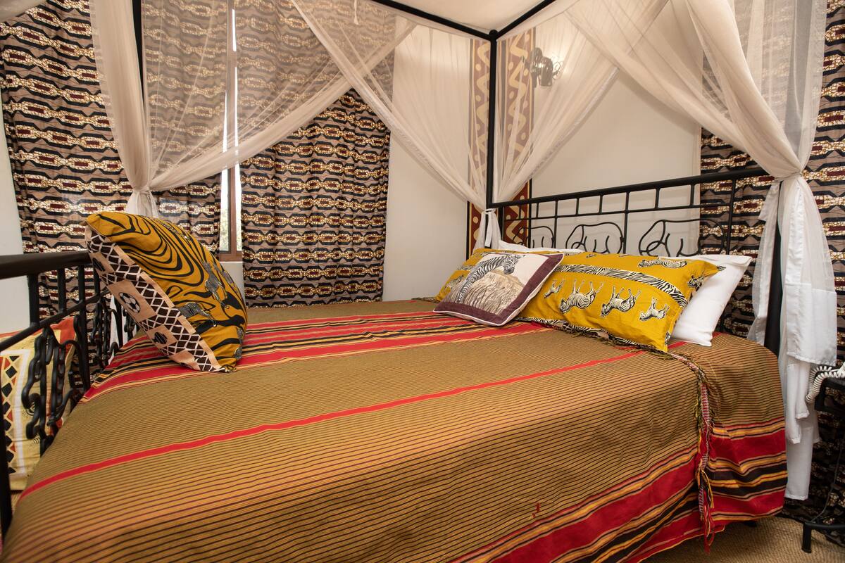 A bed with a striped bedspread, a canopy, and patterned pillows.