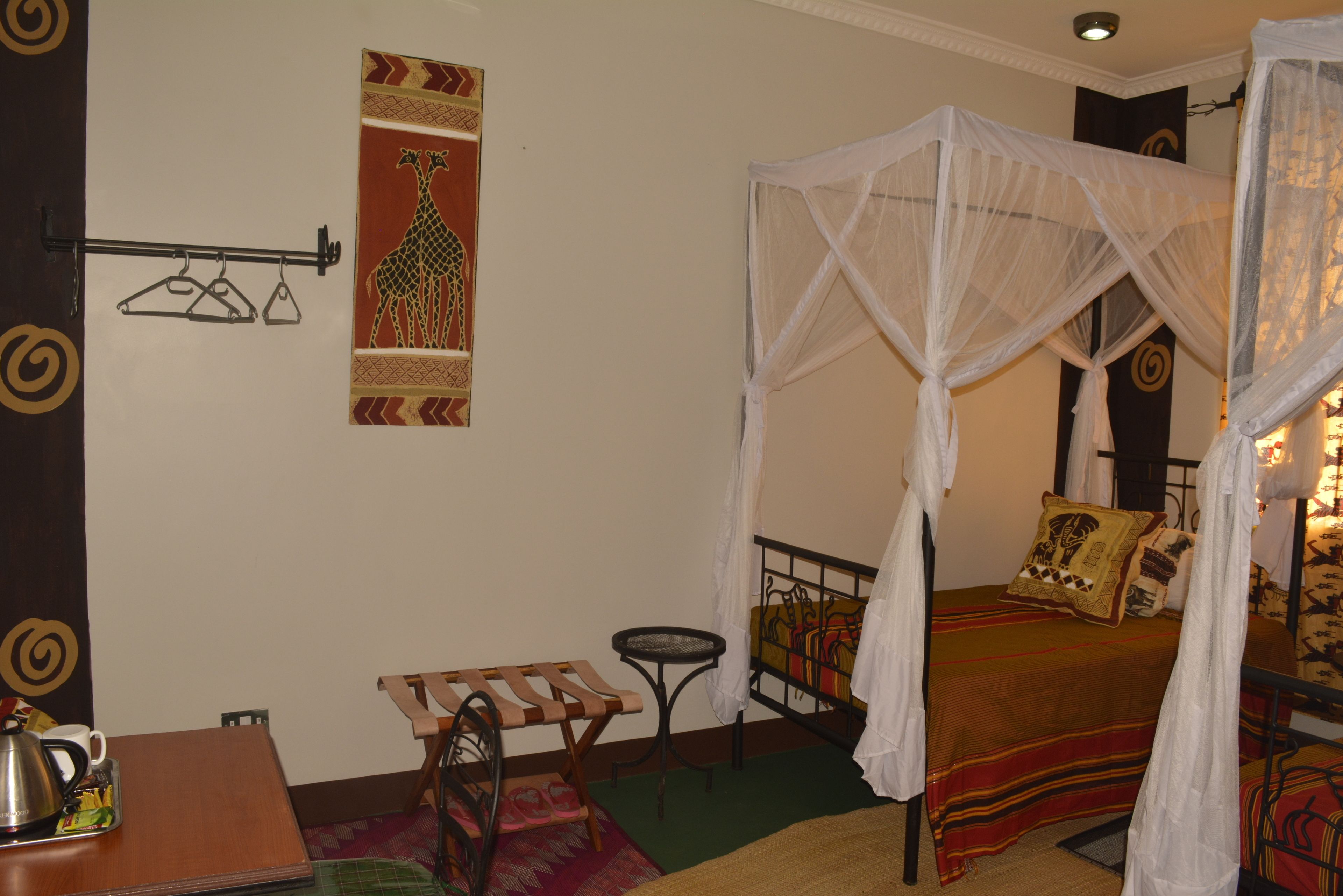 A bedroom with a bed, a small table, a chair, a hanging clothes rack, and a wall decoration.