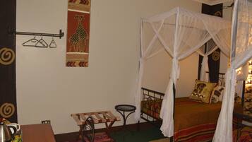 A bedroom with a bed, a small table, a chair, a hanging clothes rack, and a wall decoration.