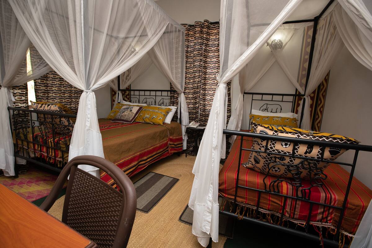 A room with two beds, each with a canopy, and a wooden table with a chair.