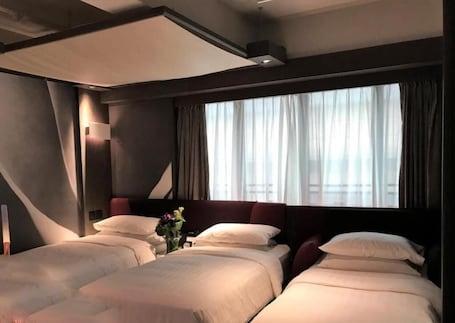 A hotel room with two beds, a large window with curtains, and a modern ceiling design.