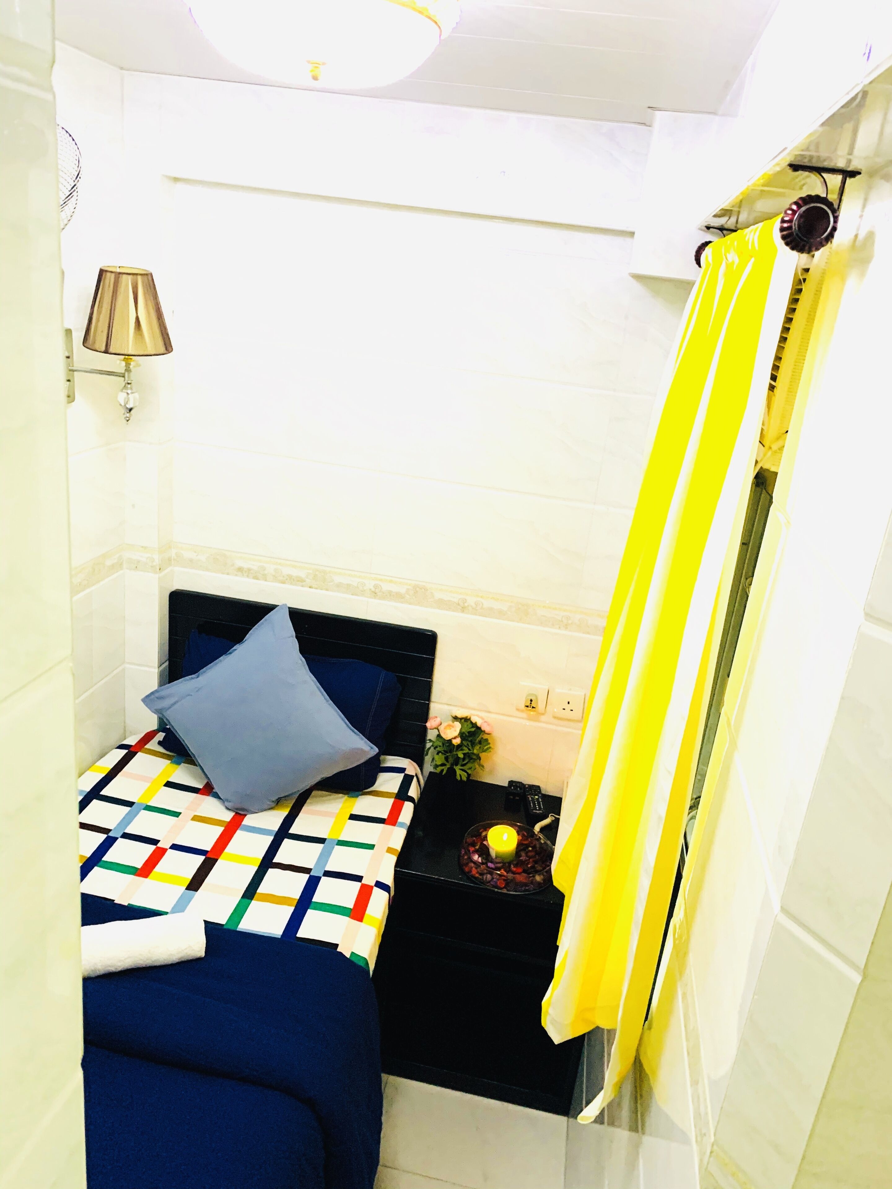 Ein kleines, gemütliches Schlafzimmer mit Bett, Nachttisch, Lampe und Duschvorhang.