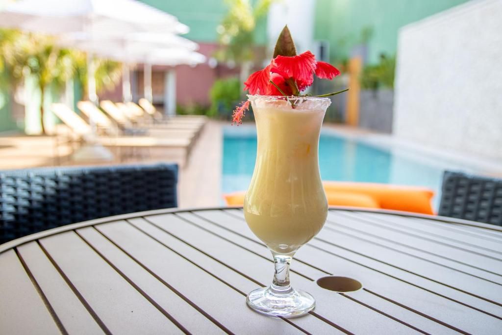 Un cocktail servi dans un verre, agrémenté d’une feuille décorative, posé sur une table au bord d’une piscine.