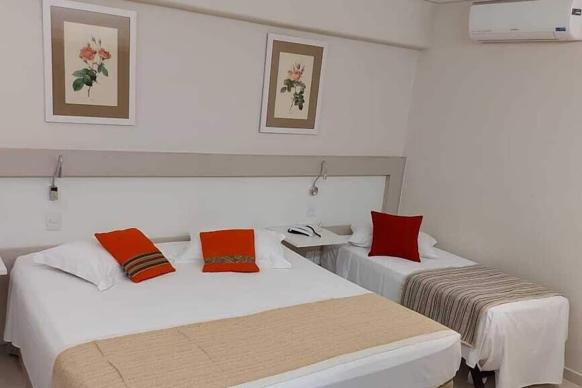 A hotel room with two beds, a small table, and an air conditioning unit.
