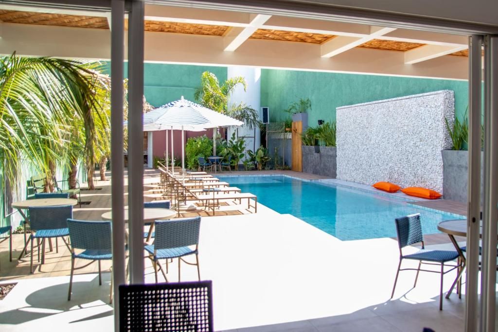 A pool area with lounge chairs and umbrellas, surrounded by greenery and a tiled floor.