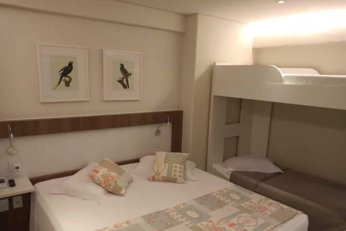 A hotel room with a bed, a bunk bed, and two framed pictures on the wall.
