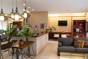 A hotel lobby with a reception desk, seating area, and a television mounted on the wall. - Lirio D'Agua Hotel (Olímpia)
