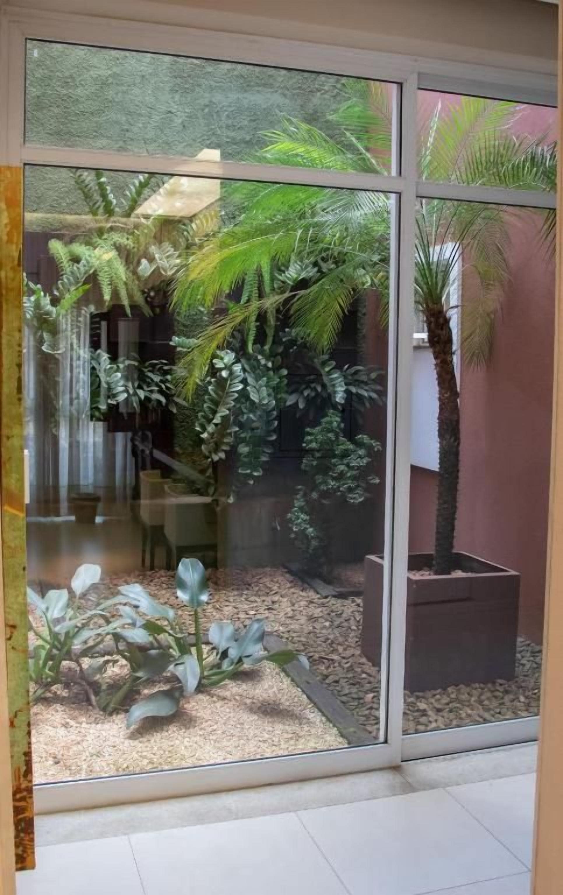 A room with a large sliding glass door leading to a garden area with various plants and a palm tree.
