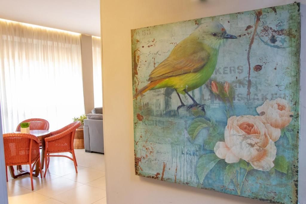 Quarto com área de jantar, mobiliário em vime e pintura de um pássaro e flores na parede.