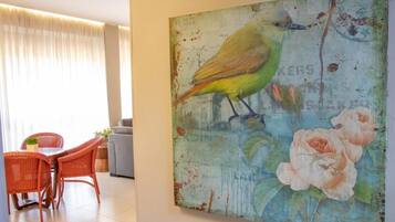 Quarto com área de jantar, mobiliário em vime e pintura de um pássaro e flores na parede.