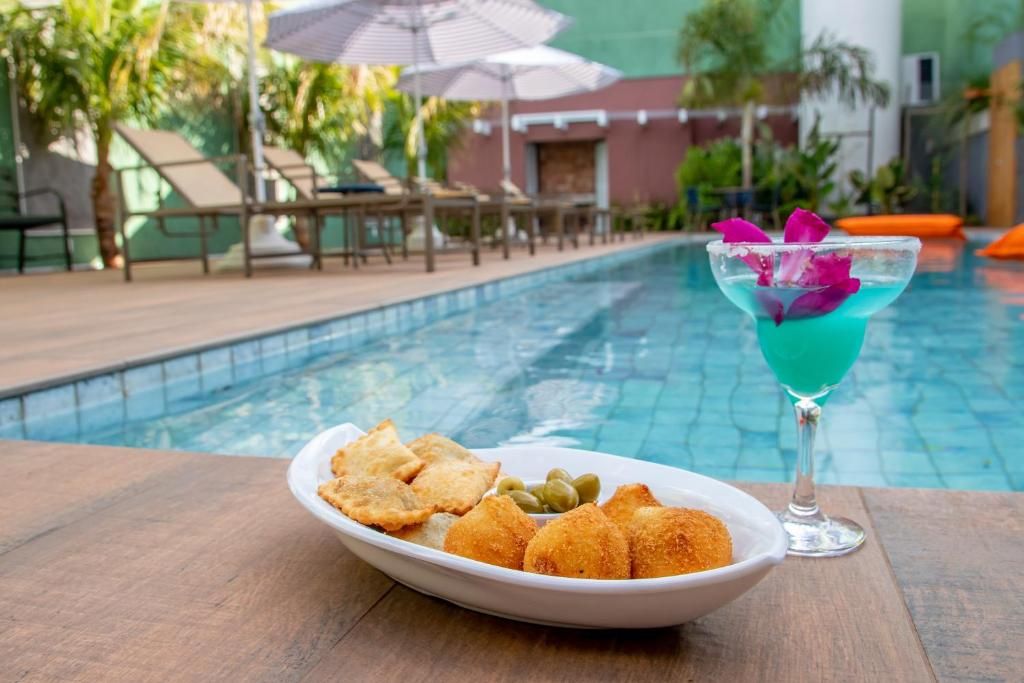 A poolside setting with a table, a plate of fried snacks, and a cocktail with a flower garnish.