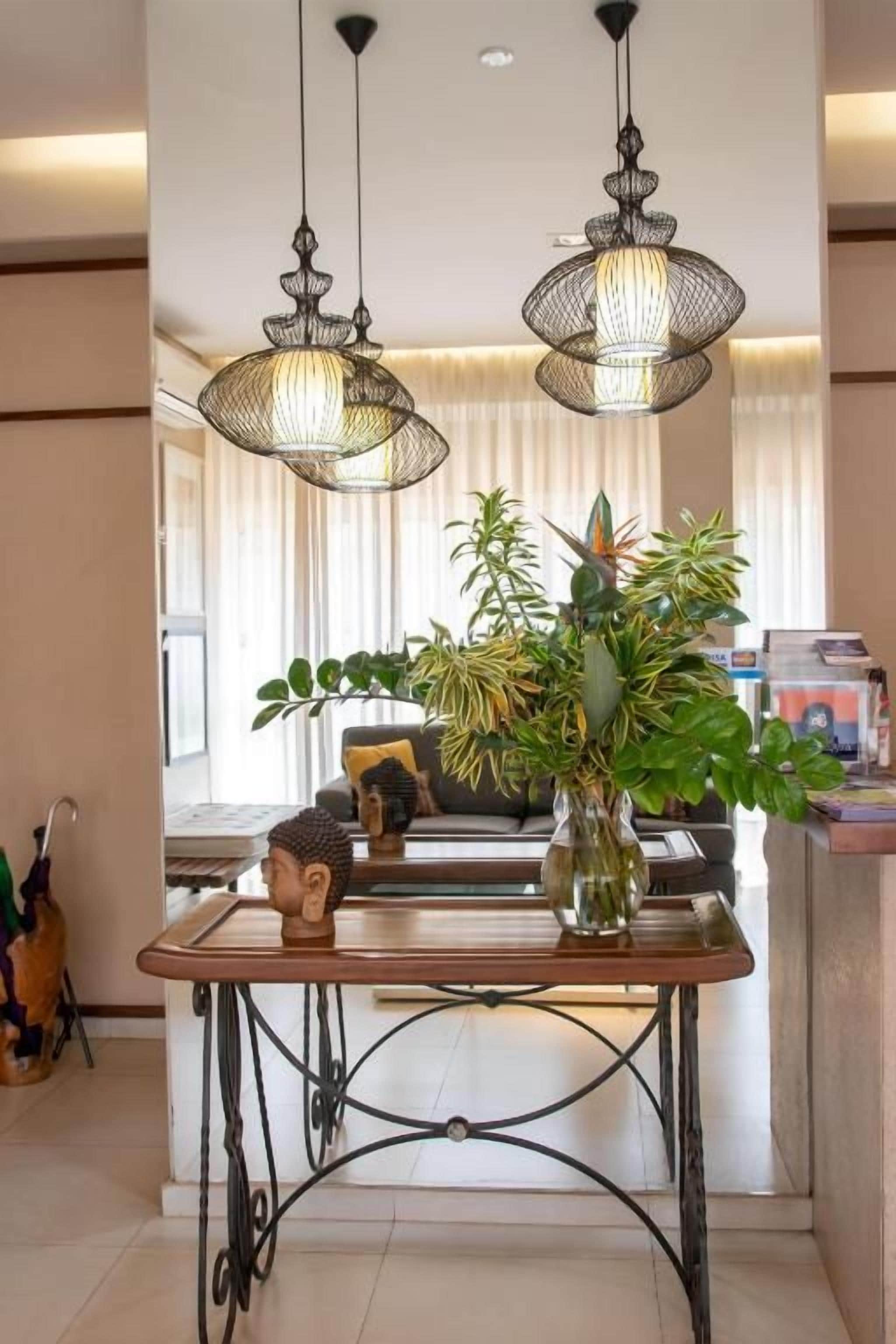 A dining area with a table, chairs, hanging lights, and a vase with plants.