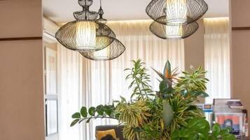 A dining area with a table, chairs, hanging lights, and a vase with plants.