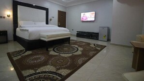Une chambre d’hôtel avec un grand lit, un téléviseur fixé au mur, un réfrigérateur et un sol recouvert de moquette.
