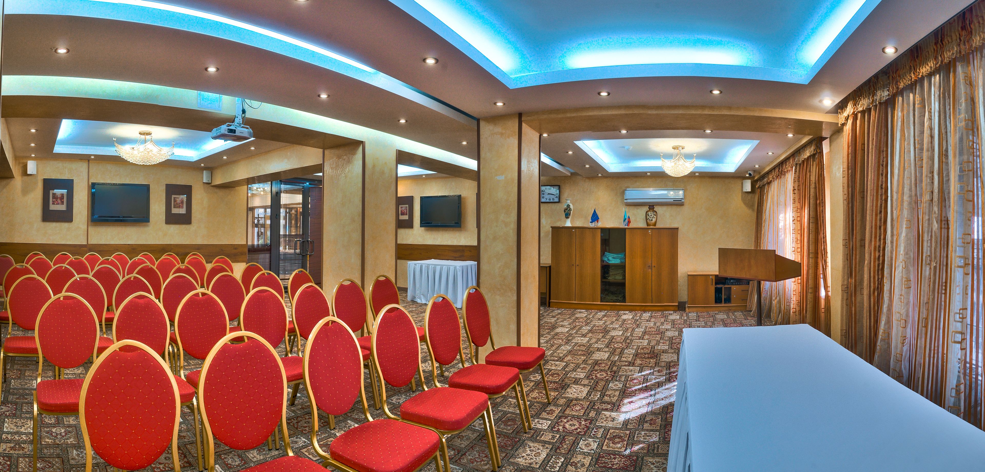 A conference room with rows of red chairs, a white table, and a chandelier.