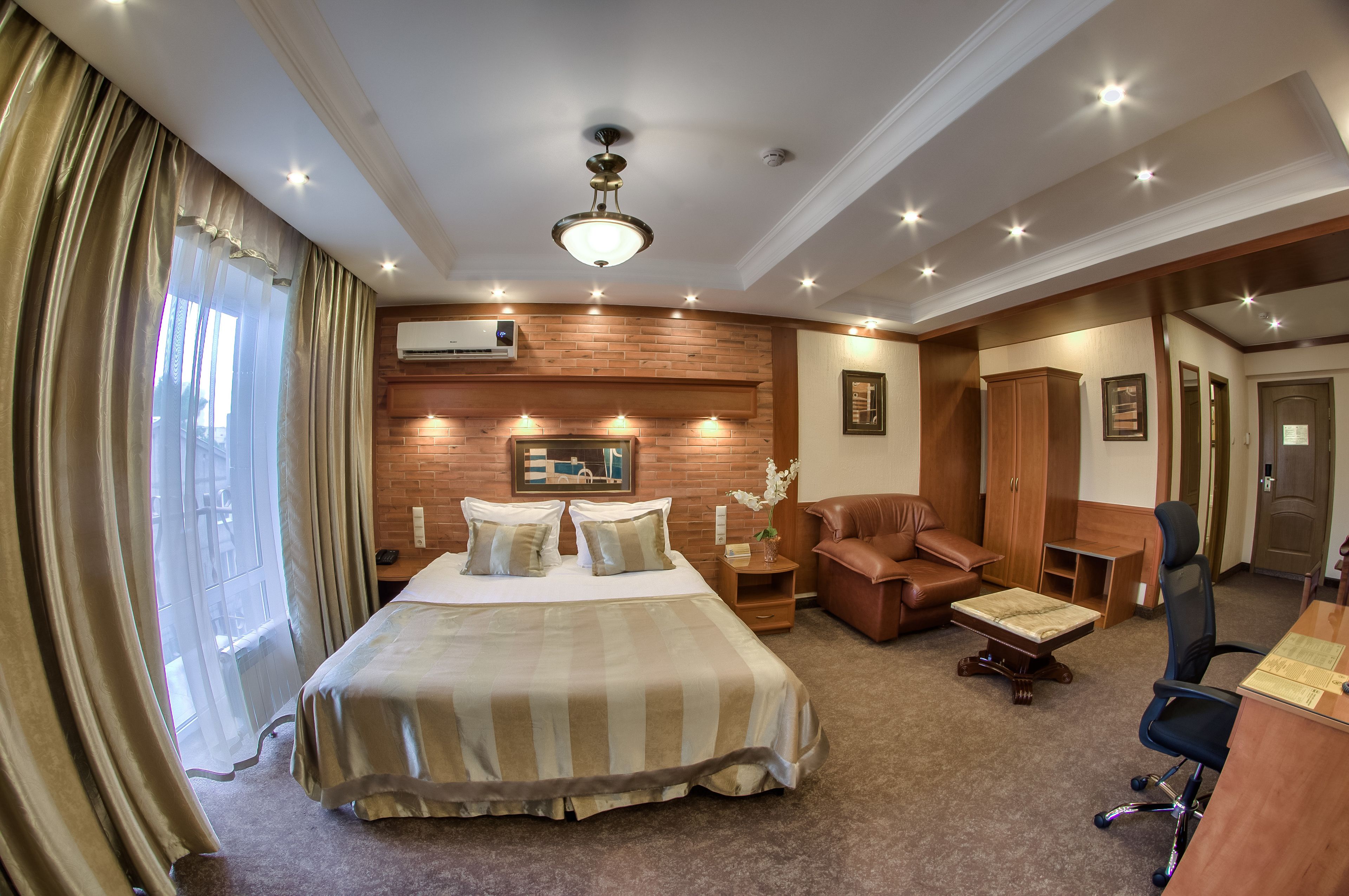 A hotel room with a large bed, a desk, a leather armchair, and a small table.