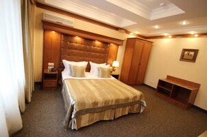 Habitación de hotel con una cama grande, cabecero de madera, mesita de noche, armario y un pequeño banco.