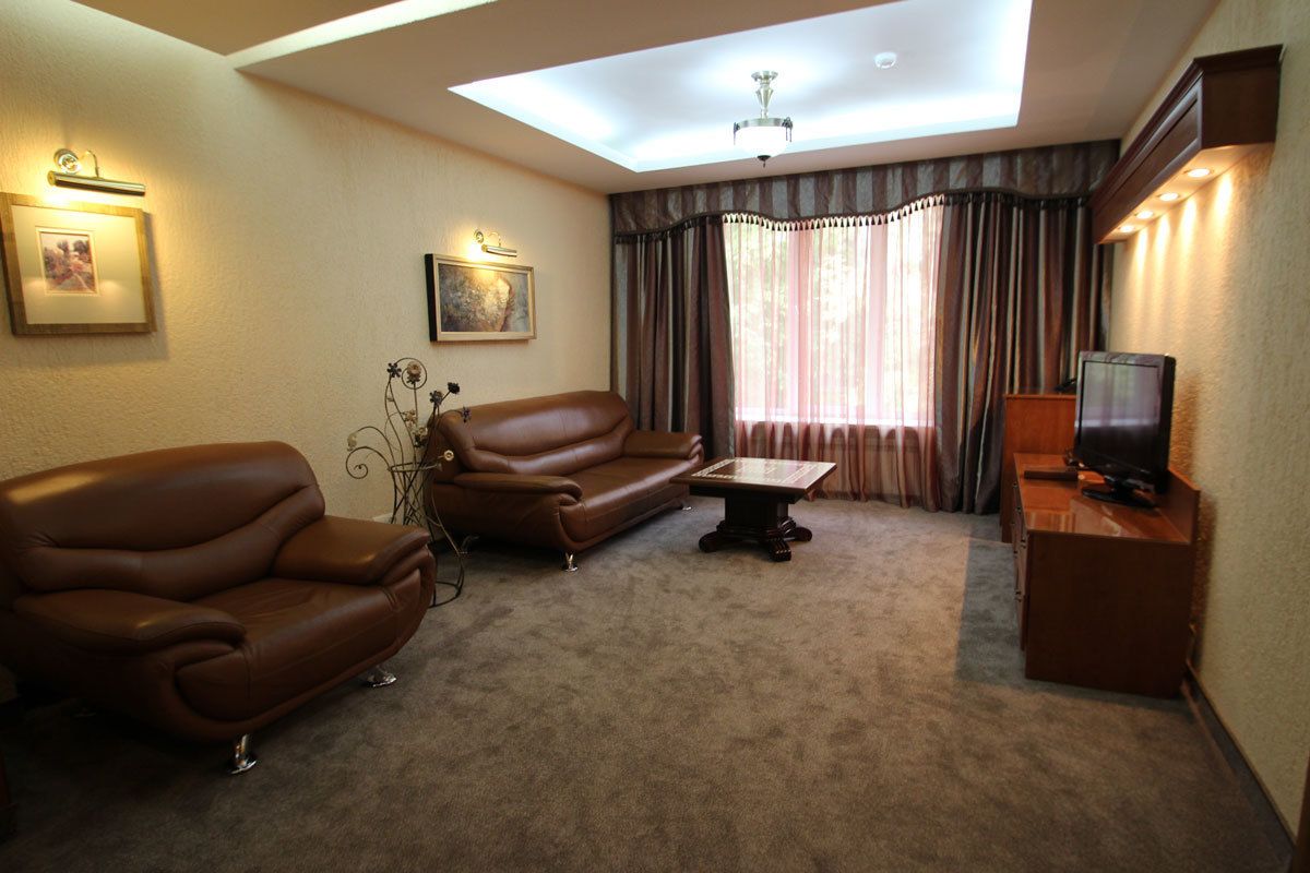 A living room with a brown leather sofa, a small table, a television on a wooden stand, and a ceiling skylight.