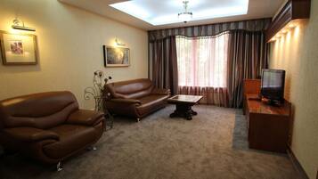 A living room with a brown leather sofa, a small table, a television on a wooden stand, and a ceiling skylight.