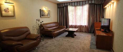 A living room with a brown leather sofa, a small table, a television on a wooden stand, and a ceiling skylight.