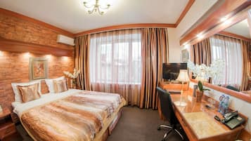 A hotel room with a large bed, a desk with a computer, a TV, and a bathroom with a shower and toilet.