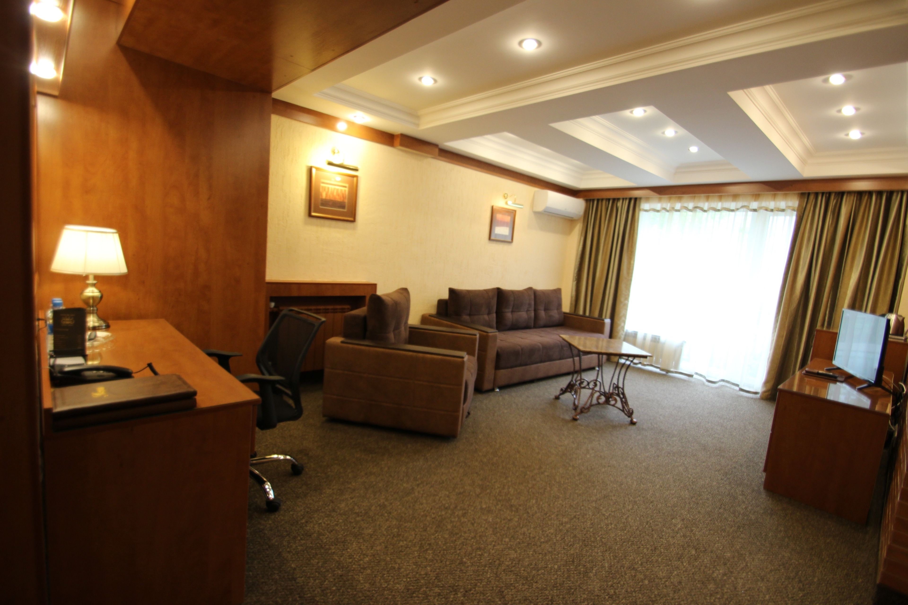 A hotel room with a wooden desk, a sofa, a small table, and a television.