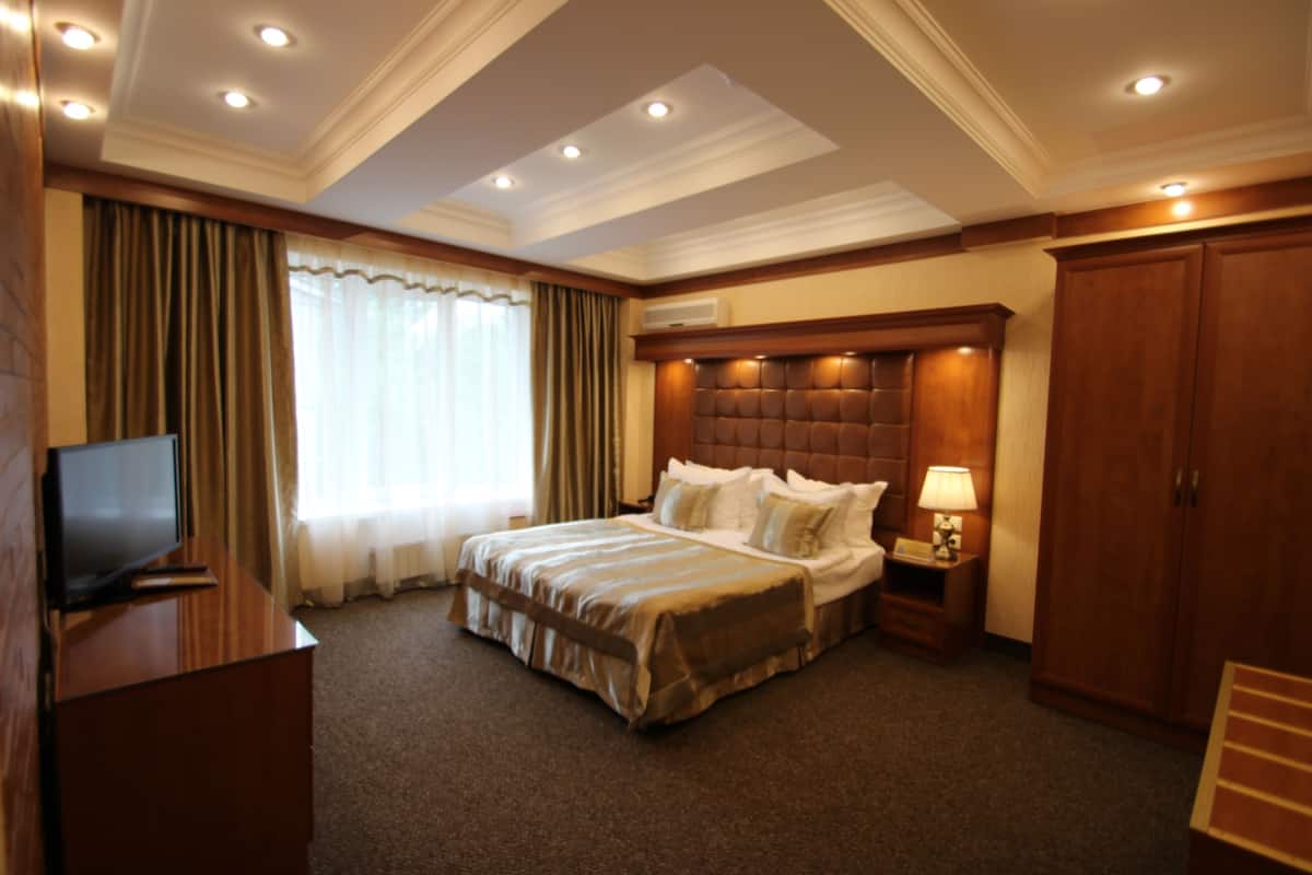 A hotel room with a large bed, a television, a nightstand with a lamp, and a wardrobe.
