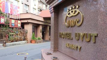 Exterior del Hotel Uyut en Almaty, con un letrero destacado que muestra el nombre del hotel y un logotipo con una corona.