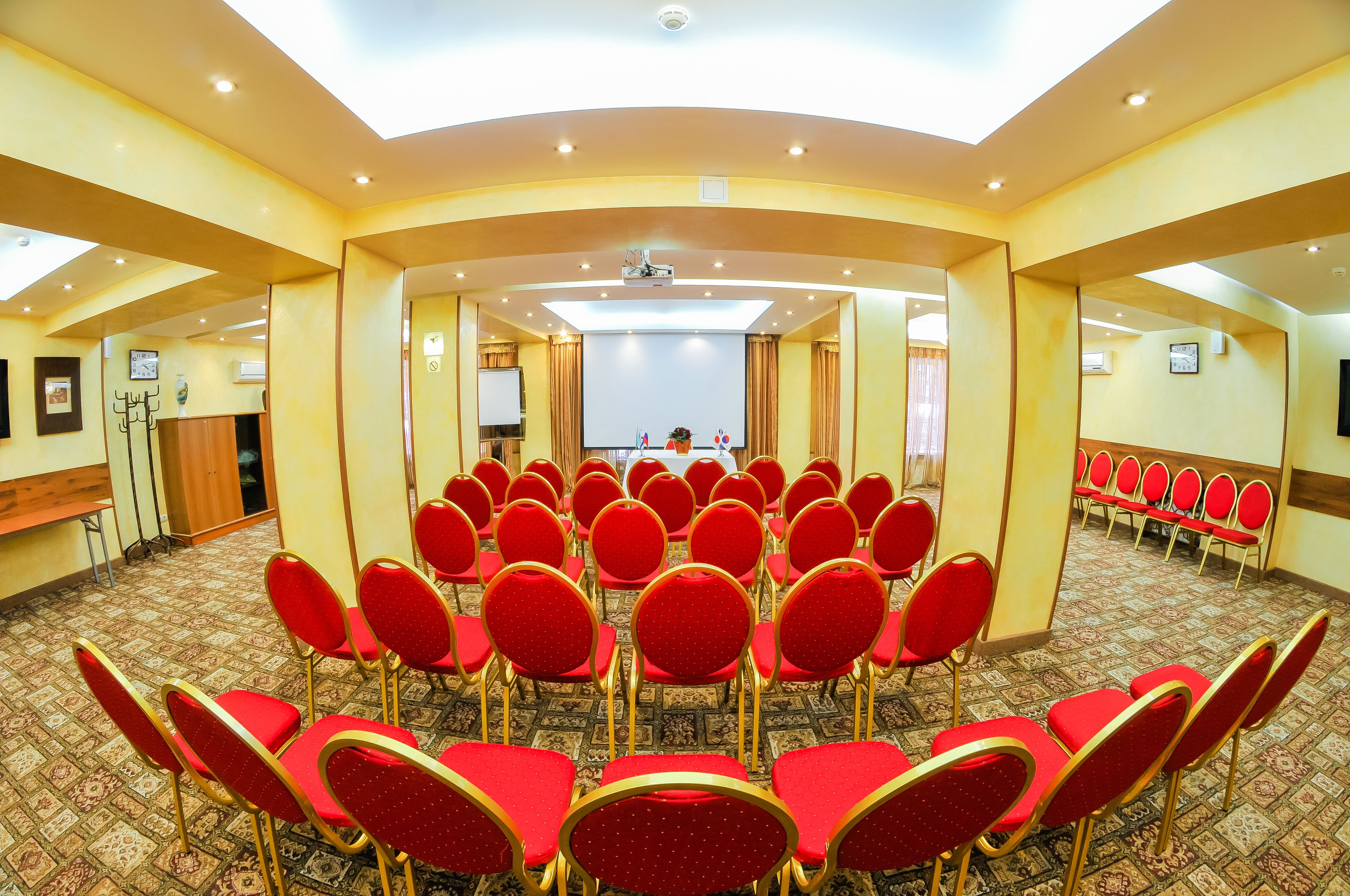 A conference room with rows of red chairs, a projector screen, and a podium.