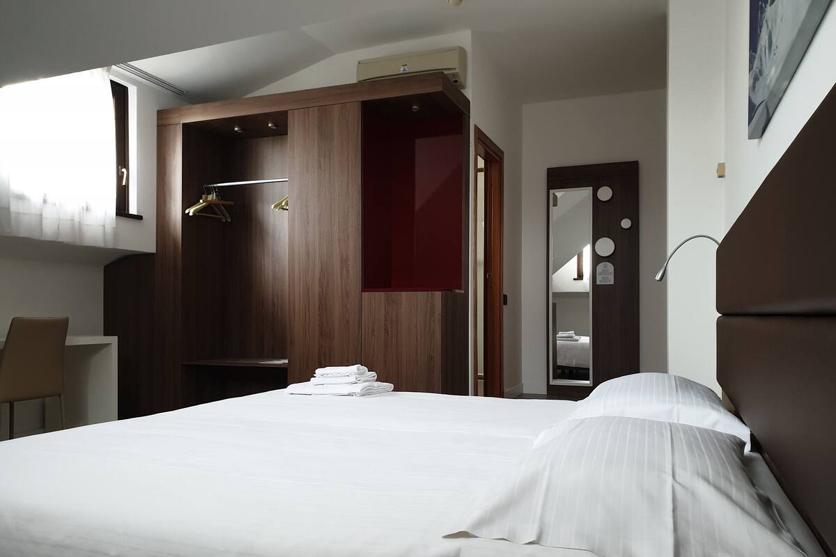 A hotel room with a bed, a desk, a wardrobe, and a mirror.