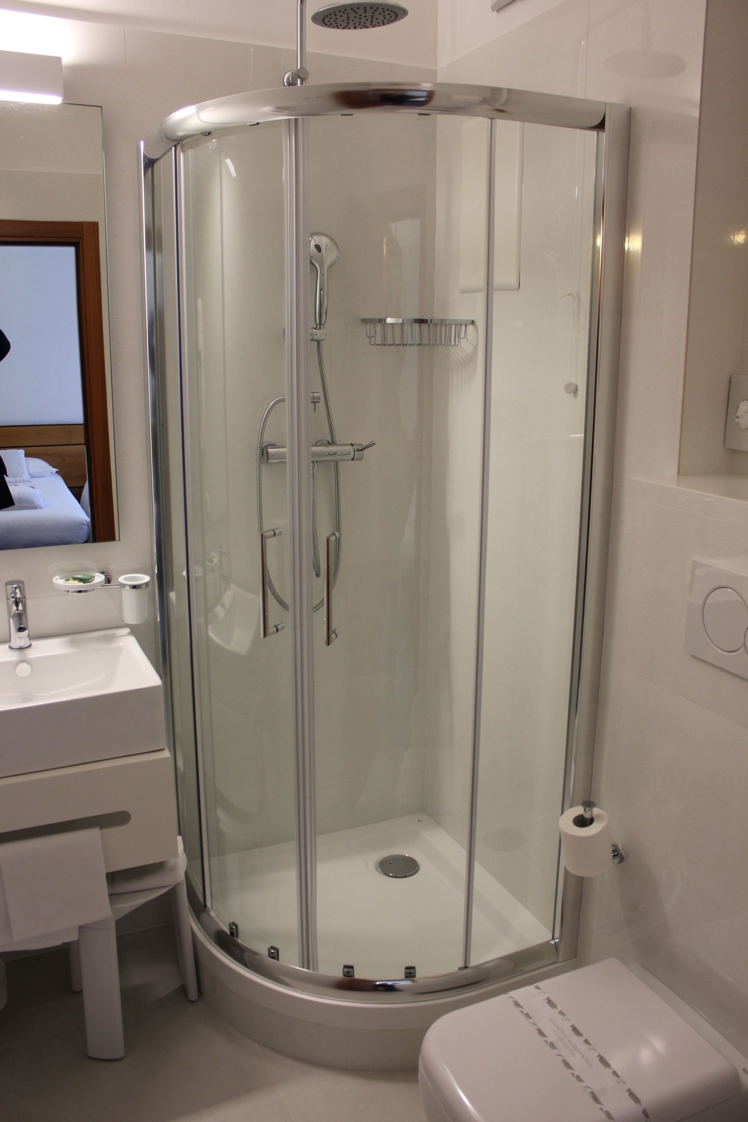 Et moderne badeværelse med et brusebad bag glas, en hvid vask og et toilet.