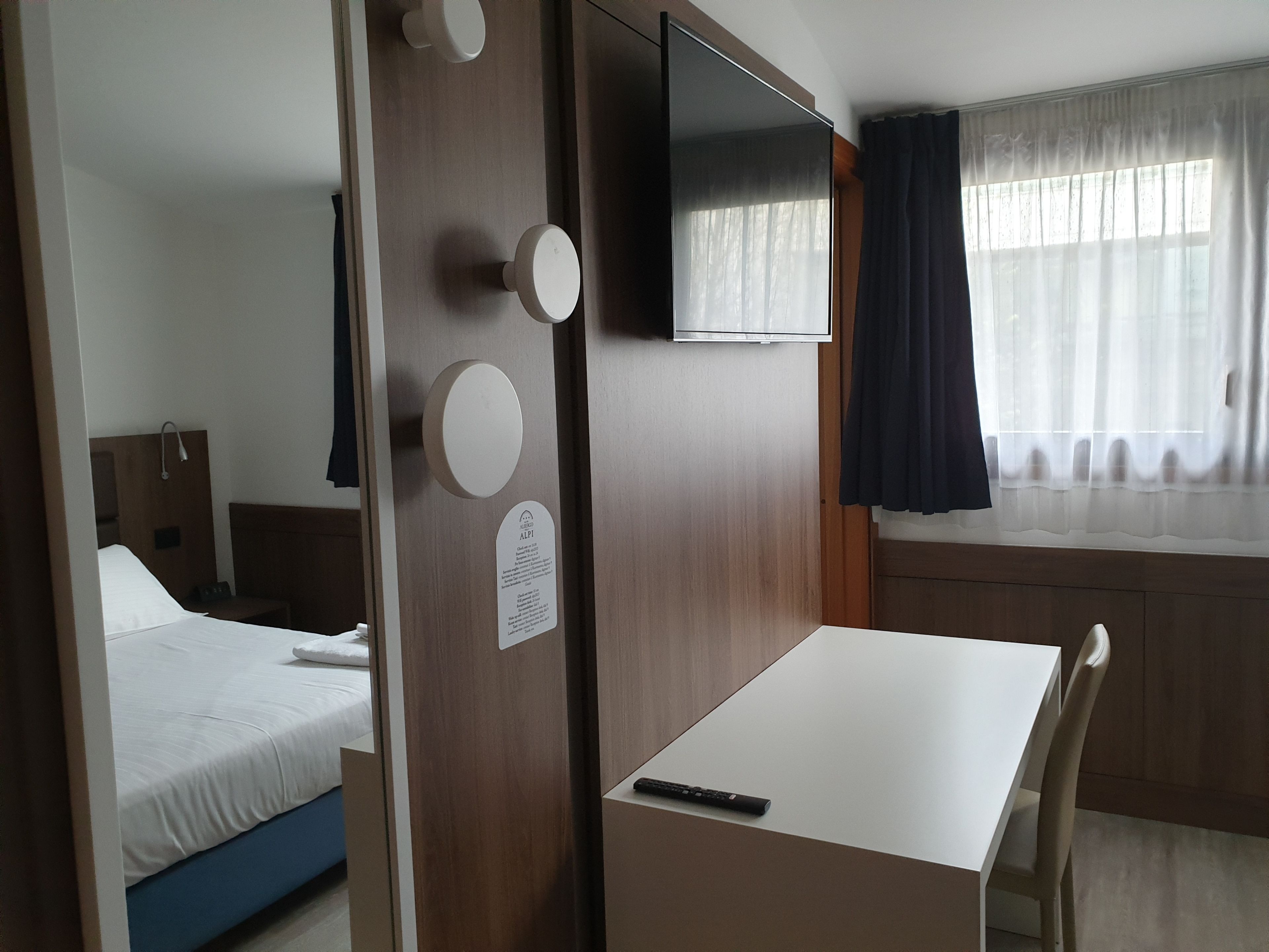 A hotel room with a bed, a desk, a chair, a TV, and a window with curtains.