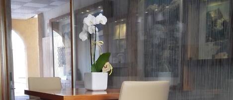 A modern interior with a glass partition, a wooden table, two chairs, and a potted orchid.