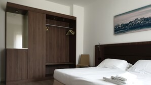 Una habitación de hotel con una cama, un armario de madera, una silla y un cuadro en la pared.