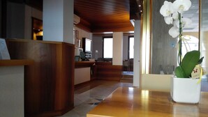 Zona de recepción con un mostrador de madera, un jarrón blanco con orquídea y vista al comedor.