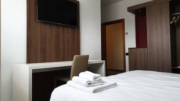Une chambre d’hôtel comprenant un lit, un bureau avec une chaise, un téléviseur fixé au mur et une armoire.