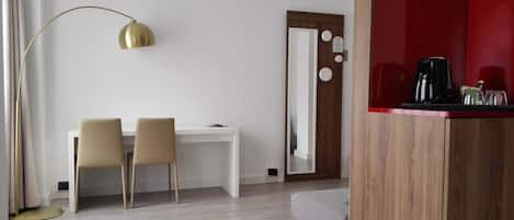 Habitación de hotel con escritorio, dos sillas, lámpara de pie, espejo y una pared de acento roja.